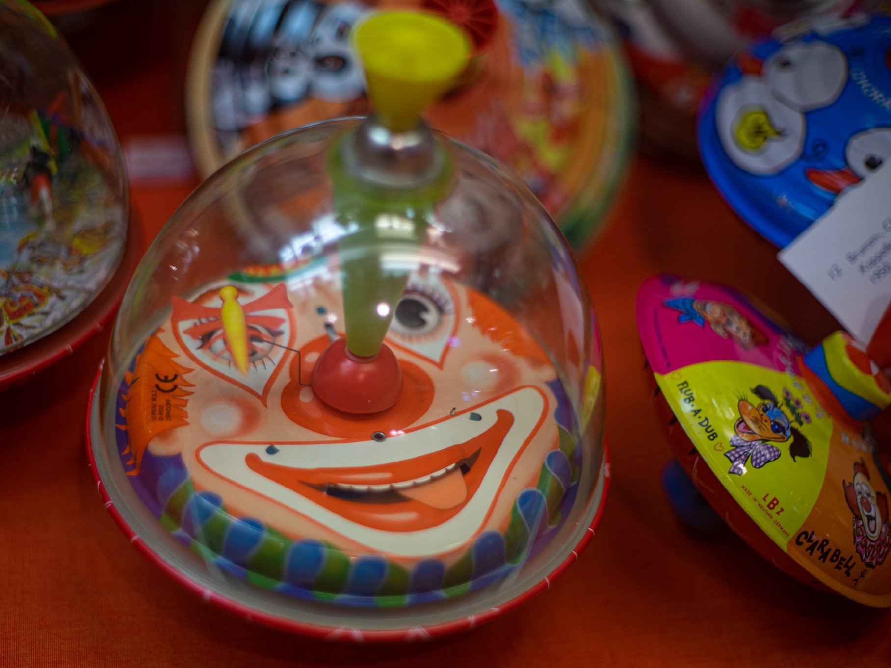 Kreisel mit einer durchsictigen Kuppel aus Plexiglas, unter der ein Clownsgesicht zu sehen ist